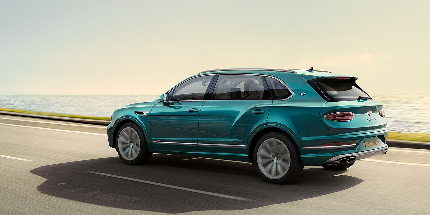 Jack Barclay Bentley Bentayga Extended Wheelbase Azure luxury SUV rear three quarter in Topaz Blue by Mulliner paint, driving on an ocean road.
