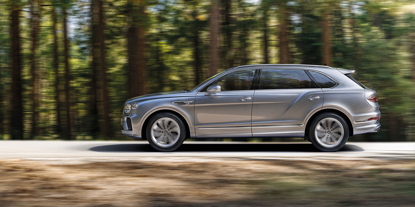Jack Barclay Bentley Bentayga luxury SUV front three quarter in Moonbeam paint, driving on an country road past trees.