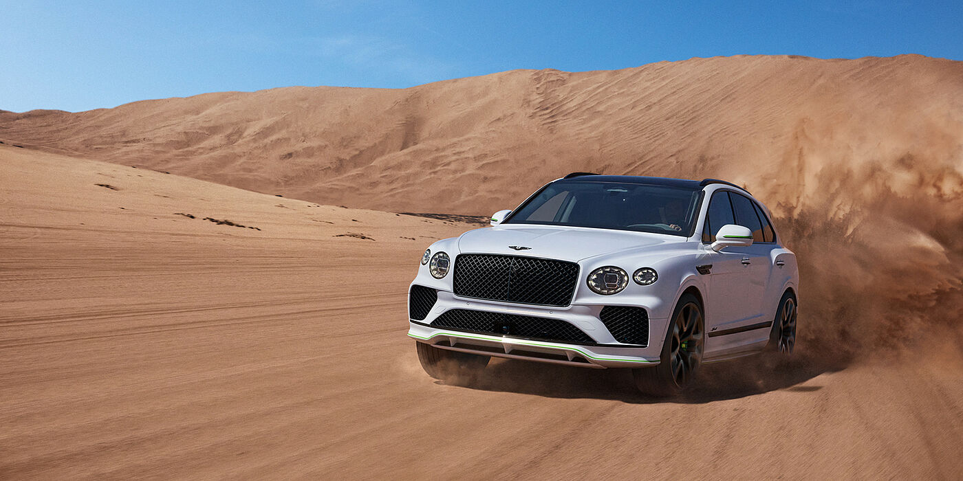 Jack Barclay Bentley Bentayga Speed SUV front three quarter in Snow Quarts Pearlescent by Mulliner white paint driving dynamically through the desert