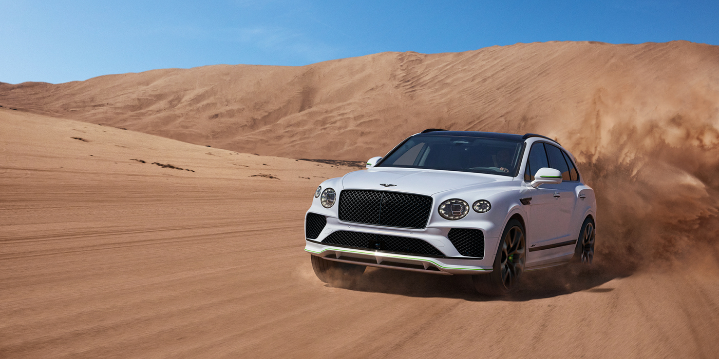 Jack Barclay Bentley Bentayga Speed SUV front three quarter in Snow Quarts Pearlescent by Mulliner white paint driving dynamically through the desert
