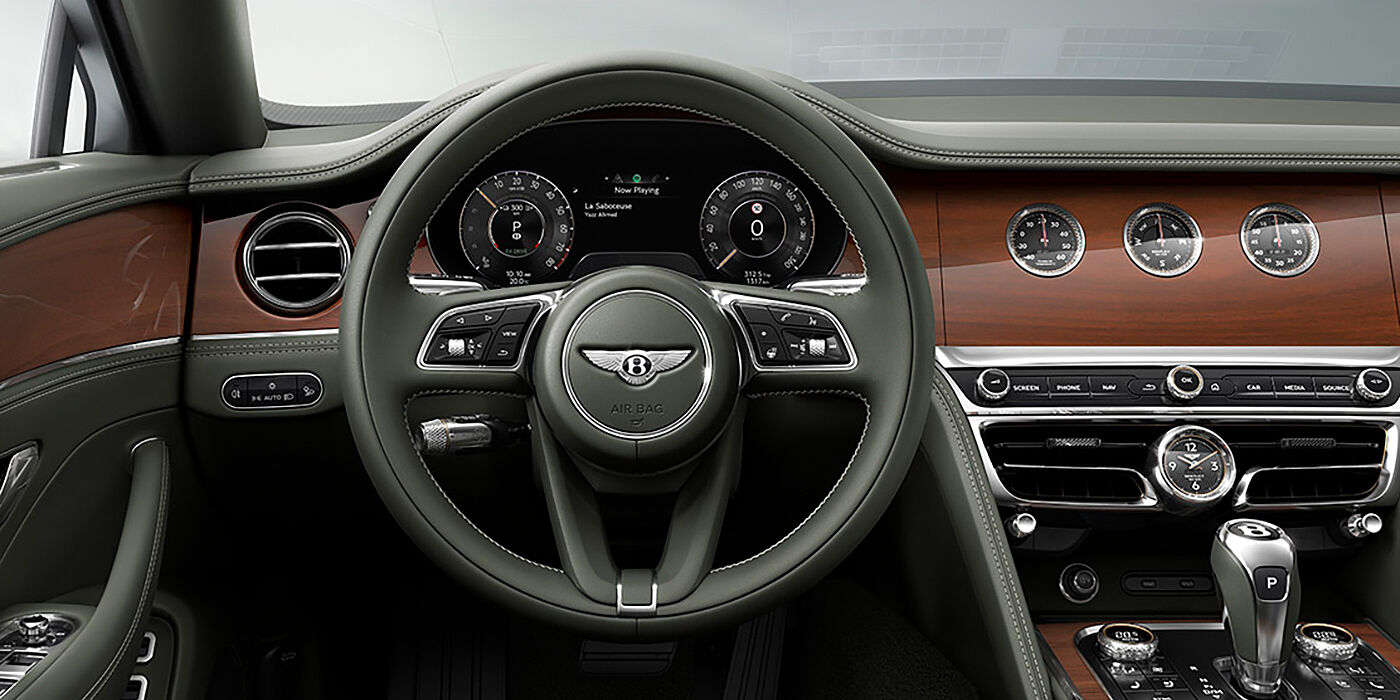 Jack Barclay New Bentley Flying Spur sedan front cabin in Cumbrian Green hide and Crown Cut walnut veneer showing steering wheel and Rotating Display with three clocks on face