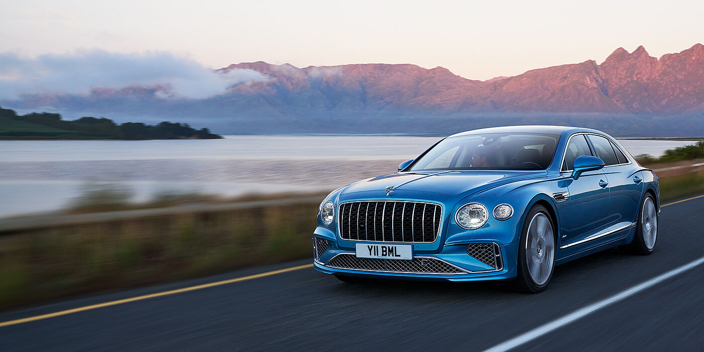 Jack Barclay New Bentley Flying Spur Azure sedan in Light windsor blue paint by Mulliner, with 22 inch Azure wheels and chrome straight vaned grille driving on a mountain road