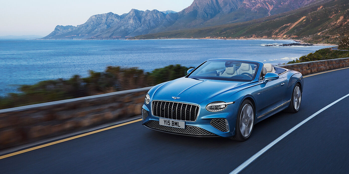 Jack Barclay New Bentley Continental GTC Azure convertible in Light Windsor blue paint with 22 inch Azure wheels and chrome grill, driving dynamically by the sea
