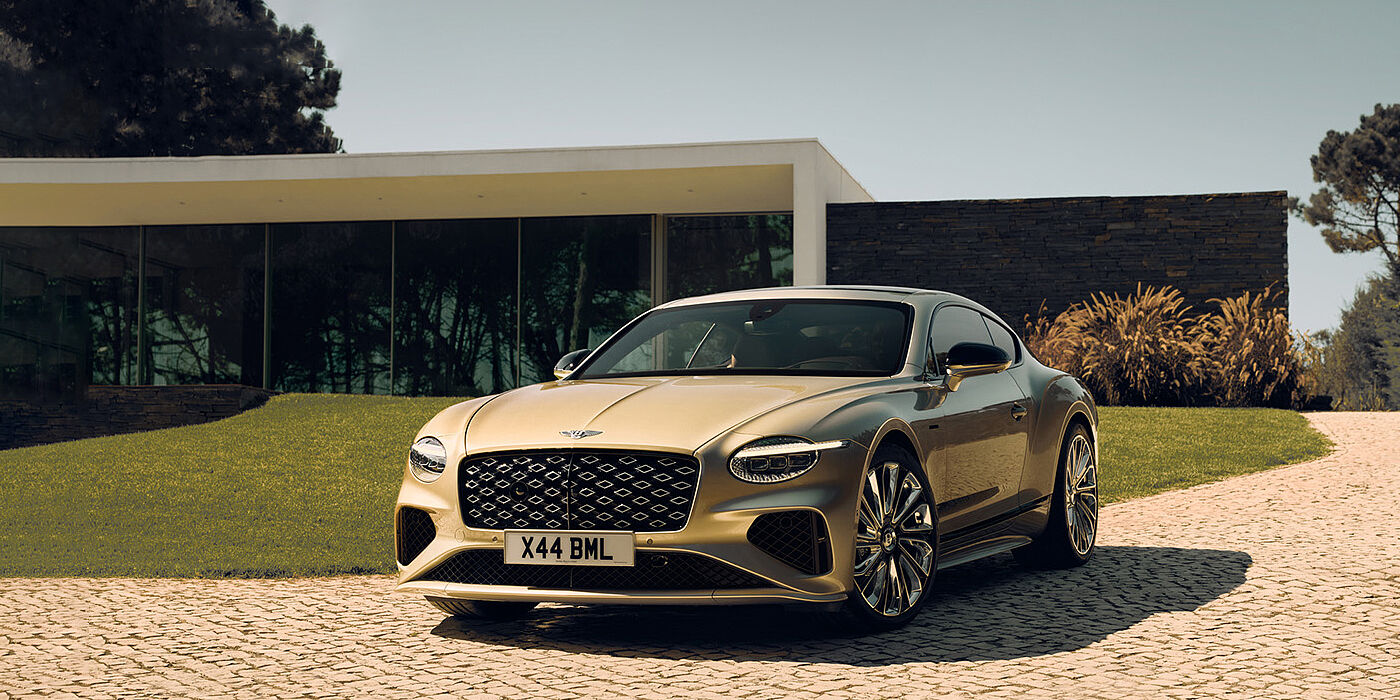 Jack Barclay Bentley Continental GT Mulliner coupe front three quarters in Patina paint parked outside a glass fronted building with a grass lawn behind it