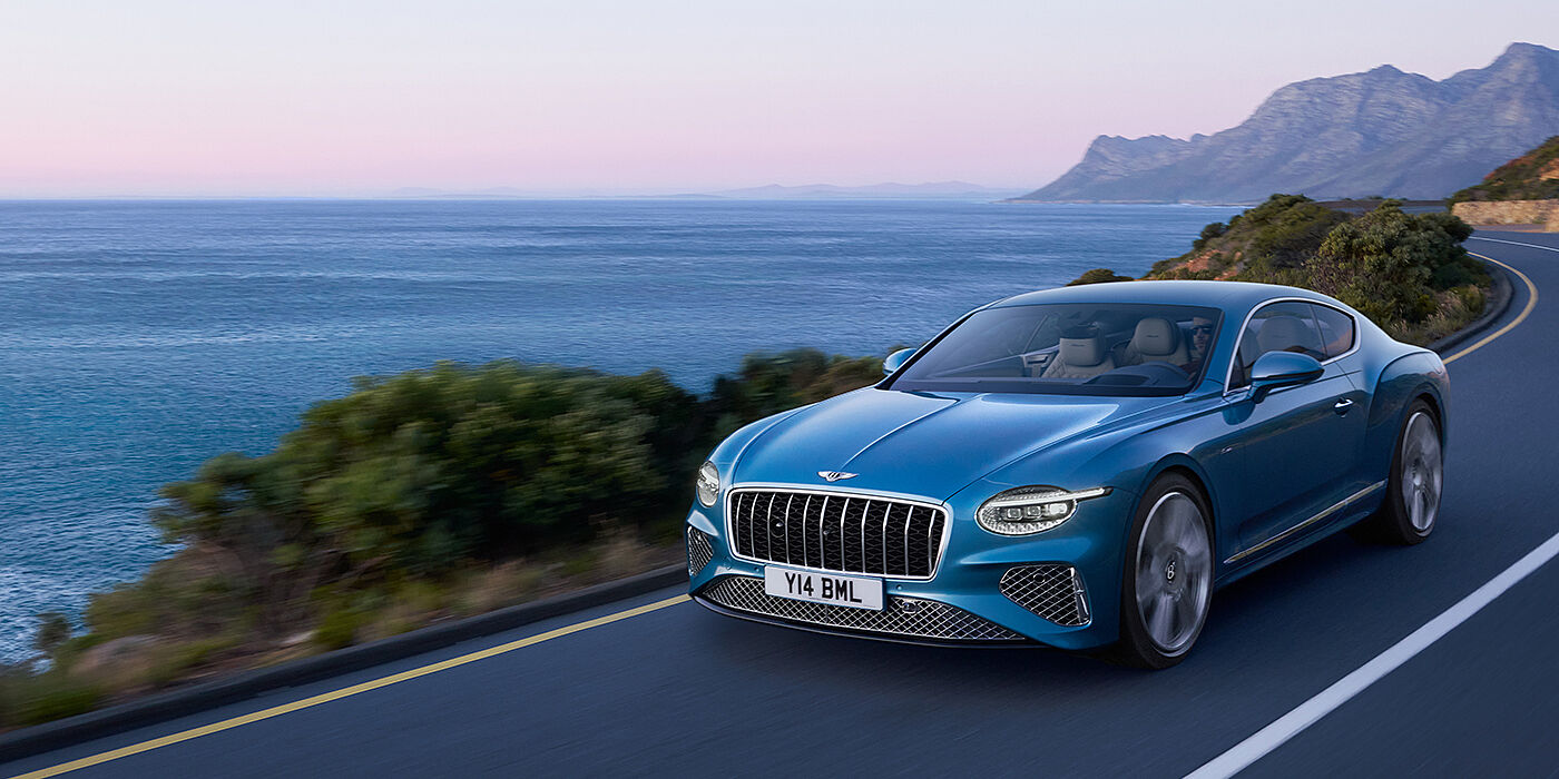 Jack Barclay New Bentley Continental GT Azure coupe in Light Windsor blue paint with 22 inch Azure wheels and chrome grill, driving dynamically by the sea