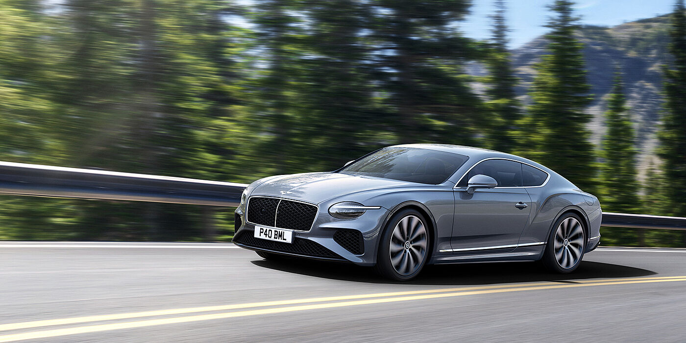 Jack Barclay New Bentley Continental GT coupe in Silverlake paint and 22 inch ten-spoke wheels, driving dynamically on a tree-lined road in the sunshine