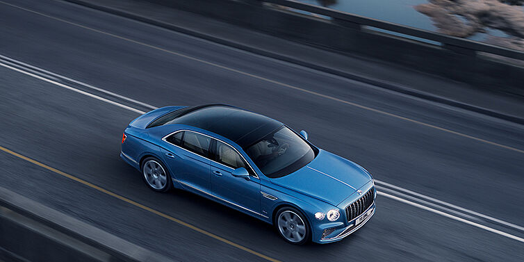 Jack Barclay New Bentley Flying Spur Azure sedan in Light windsor blue paint by Mulliner, with 22 inch Azure wheels seen from overhead driving dynamically on a country road