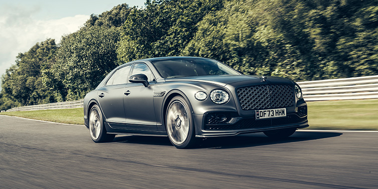 Jack Barclay Bentley Flying Spur Mulliner sedan front three quarter in dark grey paint driving dynamically by some trees on a track