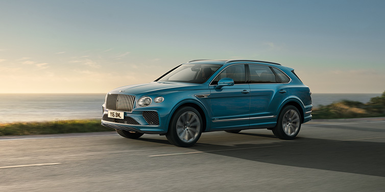 Jack Barclay Bentley Bentayga Azure SUV in Topaz blue paint driving dynamically by the ocean with 22 inch 10 spoke directional wheels