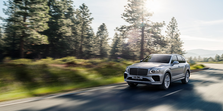 Jack Barclay Bentley Bentayga SUV front three quarter in Moonbeam silver paint driving dynamically along a tree-lined road