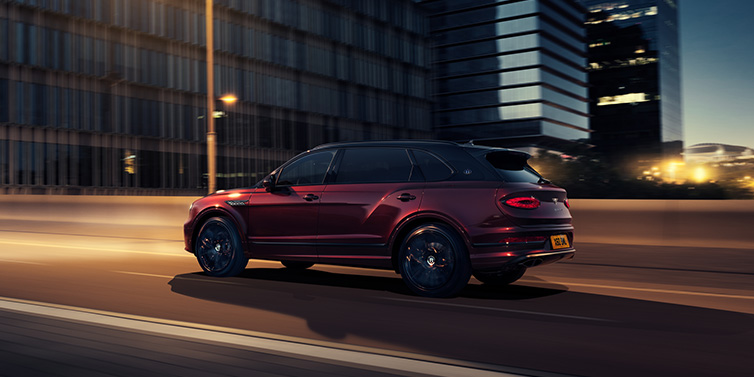 Jack Barclay Bentley Bentayga Extended Wheelbase Mulliner SUV in Cricket Ball red paint driving dynamically in city at night