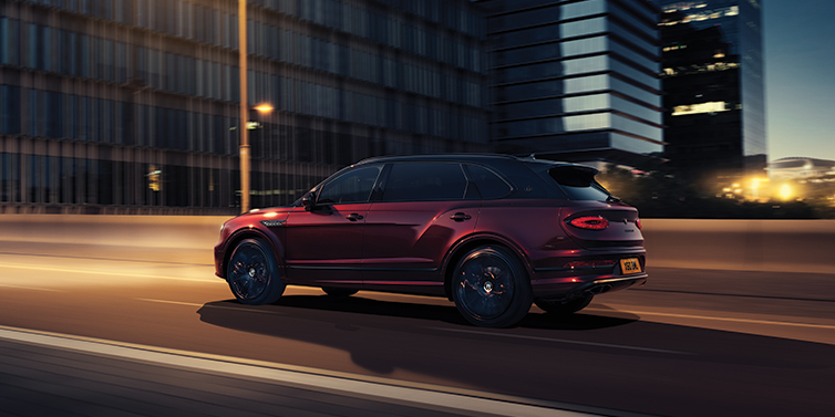Jack Barclay Bentley Bentayga Extended Wheelbase Mulliner SUV in Cricket Ball red paint driving dynamically in city at night