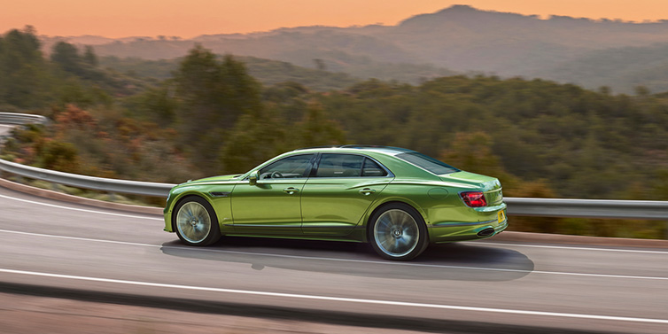 Jack Barclay Bentley Flying Spur Speed sedan side profile in Tourmaline Green paint driving dynamically on a mountain road at sunset