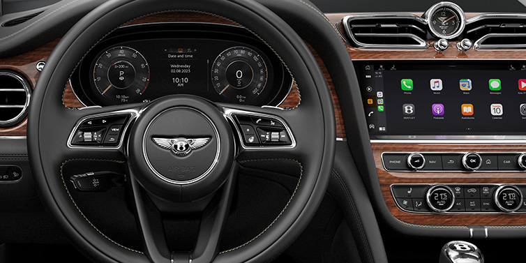 Jack Barclay Bentley Bentayga SUV front interior detail of steering wheel and driver screens surrounded by Beluga black hide and Crown Cut Walnut veneer